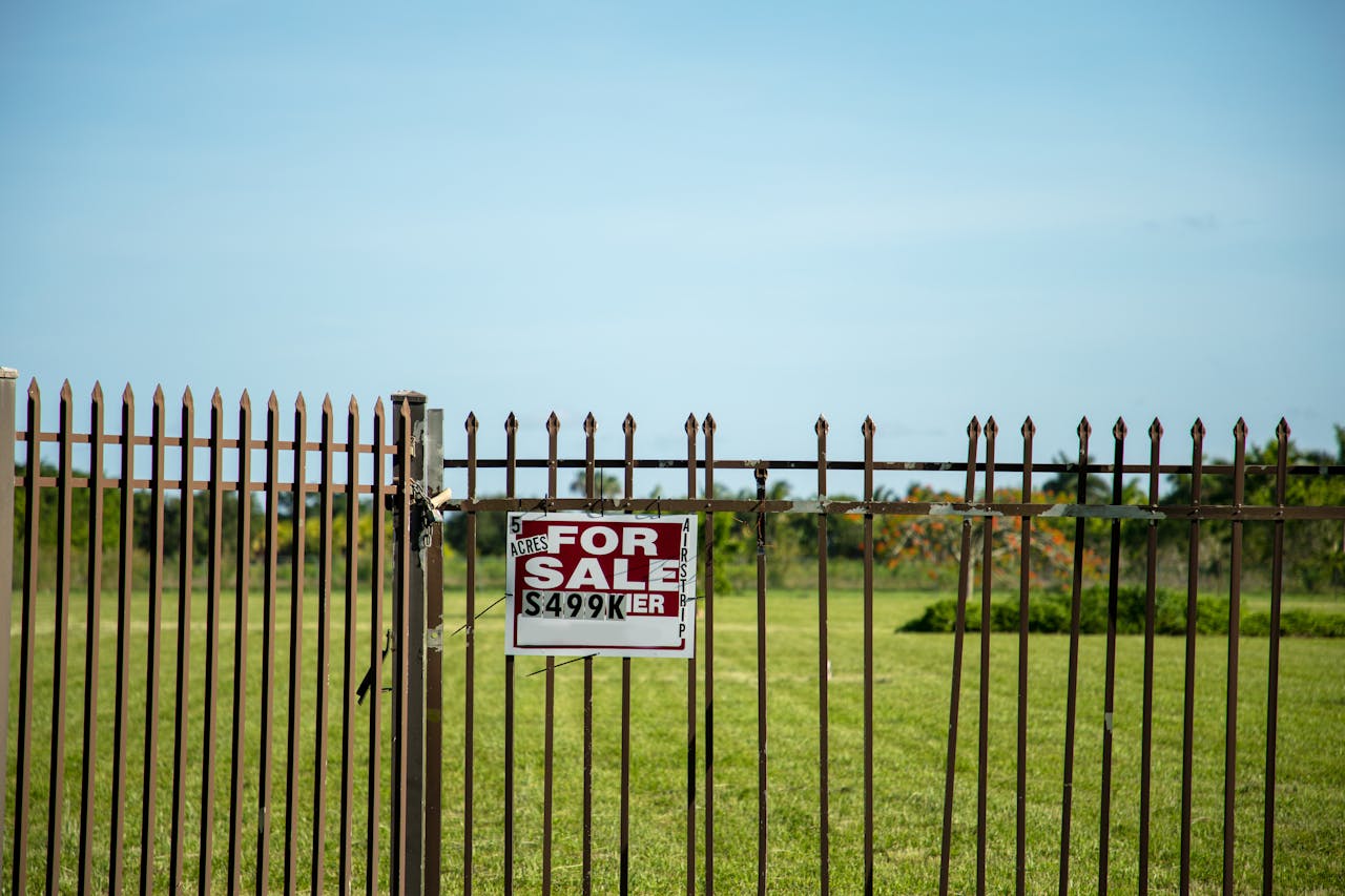 Services-01 A large plot of land bordered by an iron fence, complete with a 'For Sale' sign in Miami, FL. Ideal for development.