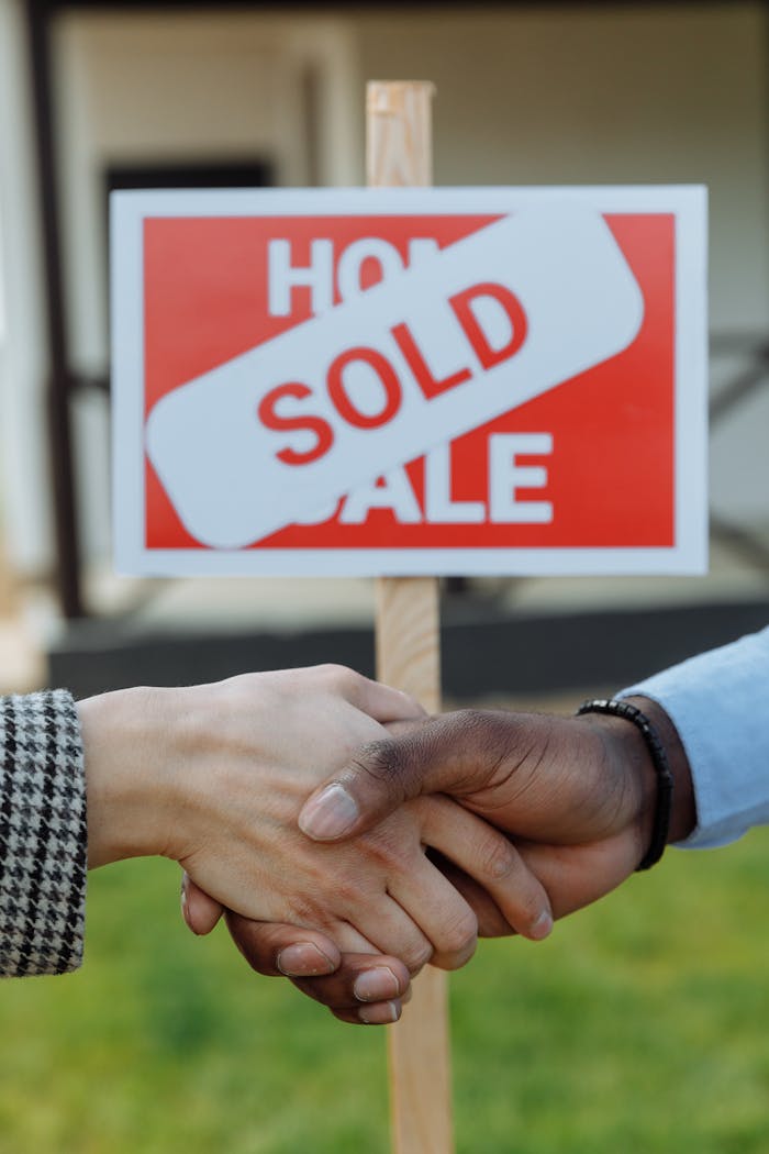 creative Close-up of a handshake in front of a sold sign symbolizing a successful real estate transaction.